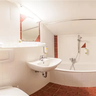 Ein modernes Badezimmer mit einer Badewanne und einer Dusche. Die Wände sind in hellen Fliesen gehalten, und es gibt Handtücher sowie Spiegel.