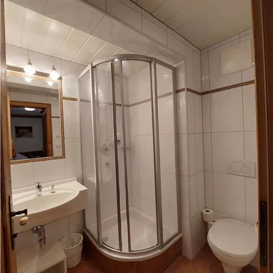 Ein modernes Badezimmer mit einer Duschkabine und einem Waschbecken. Es ist hell erleuchtet und verfügt über weiße Fliesen.