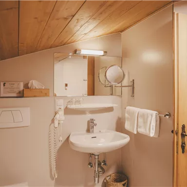 Ein modernes Badezimmer mit Holzdecke und sanitären Einrichtungen. Es gibt einen Spiegel, Handtücher und eine Tür aus Holz.