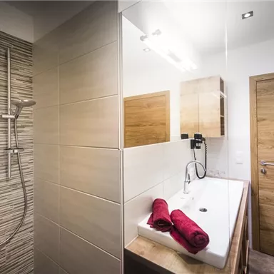 A modern bathroom with a stylish shower and a sink. Red towels are neatly placed on the shelf.