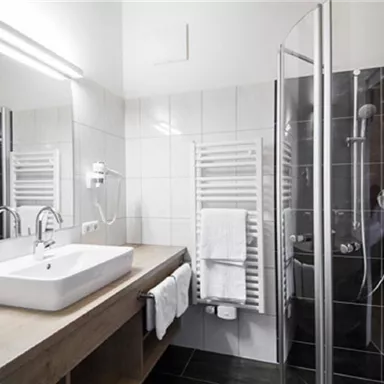 A modern bathroom with a shower and a sink. The walls are bright, and the fittings are elegant and functional.