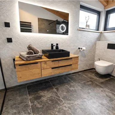 Ein modernes Badezimmer mit einer eleganten Holzwaschtischplatte und einem großen Spiegel. Die Wände sind neutral gehalten, und es gibt große Fenster, die viel Licht hereinlassen.