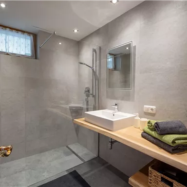 A modern bathroom with tiled floors and a spacious shower. On the shelf are towels and flowers that create a cozy atmosphere.