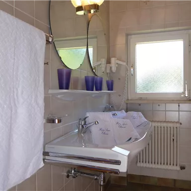 A modern bathroom with a sink, towels, and a large mirror. There are windows that let in natural light.