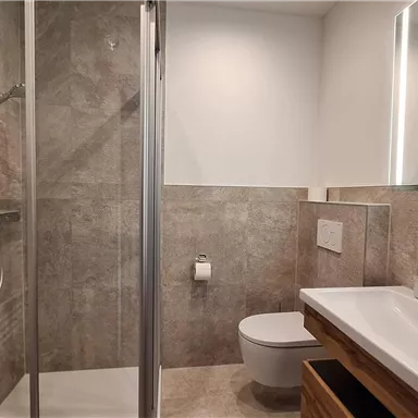 A modern bathroom with a glass shower and an elegant sink. The walls are in neutral earth tones and there is plenty of light through large windows.