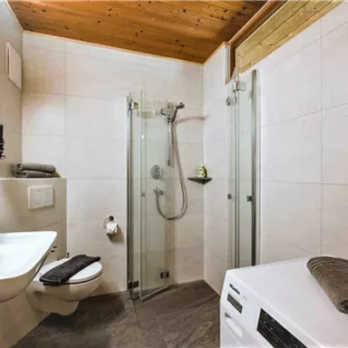 A modern bathroom with a shower and a sink. There are bright tiles and a wooden ceiling that creates a cozy atmosphere.