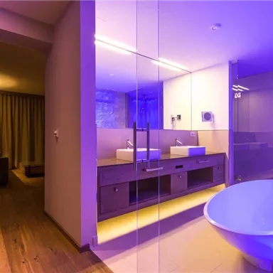 A modern bathroom with a freestanding bathtub and two sinks. The space has stylish lighting and wooden flooring.