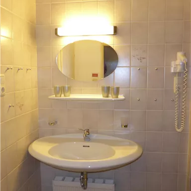 A simple bathroom with a round mirror above a sink. The walls are tiled and the light is wall-mounted.