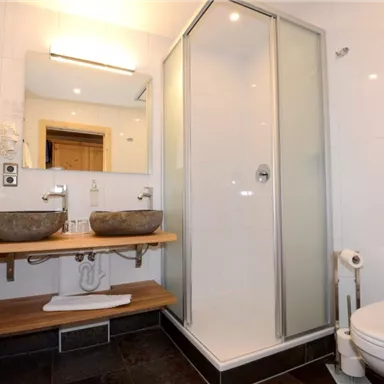 Ein modernes Badezimmer mit einer Duschkabine und zwei Waschbecken. Es kombiniert funktionales Design mit eleganten Holz- und Flieselementen.