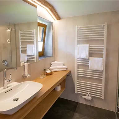 A modern bathroom with a large mirror and a sink made of white porcelain. Towels and a towel warmer are also visible.