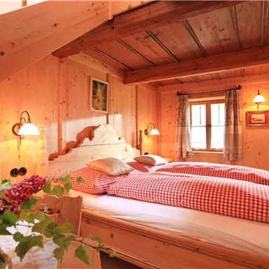 Ein gemütliches Schlafzimmer mit Holzvertäfelung und einem großen Bett. Die Einrichtung ist rustikal und einladend, mit roten karierten Bettbezügen und einer schönen Blumenpflanze im Vordergrund.