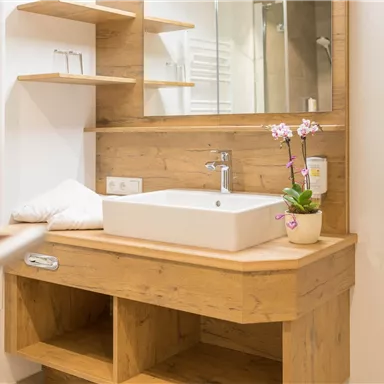 Ein modernes Badezimmer mit Holzregalen und einem eleganten Waschbecken. Ein kleiner Blumentopf mit einer Orchidee verleiht dem Raum eine angenehme Atmosphäre.