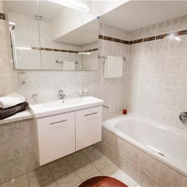 Ein modernes Badezimmer mit einer Badewanne und einem Waschbecken. Die Wände sind mit hellen Fliesen dekoriert, und es gibt einige Handtücher.