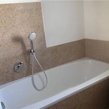 A bathroom with a white bathtub and a modern shower. The walls are clad in a simple, light material.