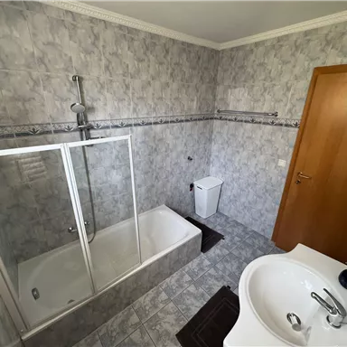 Ein modernes Badezimmer mit einer Badewanne und Duschkabine. Die Wände sind in grauen Fliesen gestaltet, und es gibt ein Waschbecken sowie eine Toilette.