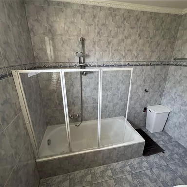 Ein Badezimmer mit einer Badewanne und Duschkabine. Die Wände sind mit grauen Fliesen gefliest.