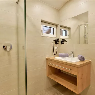 Ein modernes Badezimmer mit einer begehbaren Dusche und einem Holzwaschtisch. Die Wände sind in neutralen Farben gehalten, und es gibt frische Handtücher.