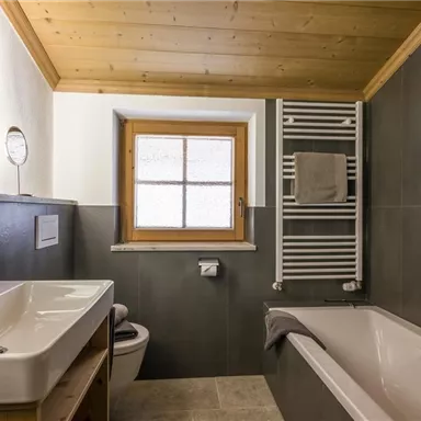 Ein modernes Badezimmer mit einer Badewanne und einem Waschbecken. Große Fenster sorgen für viel Tageslicht und eine ansprechende Atmosphäre.