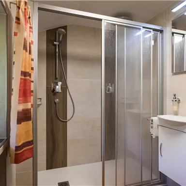 Ein modernes Badezimmer mit einer Glasdusche und einem Waschbecken. Der Raum ist hell und gut ausgestattet.