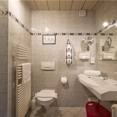 Ein modernes Badezimmer mit grauen Fliesen und einer Dusche. Es enthält ein Waschbecken, eine Toilette und Handtücher.