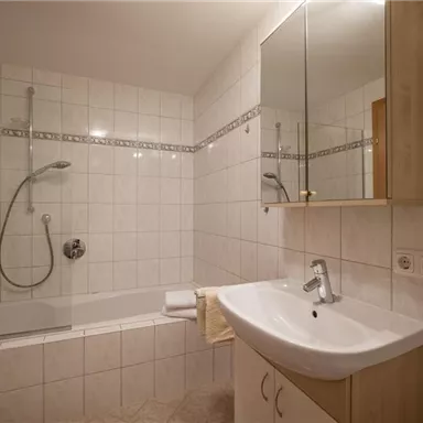 A modern bathroom with a bathtub and shower. Bright tiles and a large mirror complement the design.