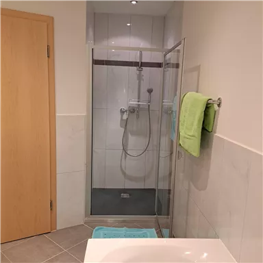 Ein modernes Bad mit einer Glasdusche und hellen Fliesen. Ein Handtuch in frischem Grün hängt neben der Dusche.