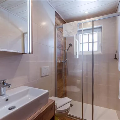 Ein modernes Badezimmer mit einer Glasdusche und einem eleganten Waschbecken. Helle Fliesen und Holzdetails schaffen eine einladende Atmosphäre.