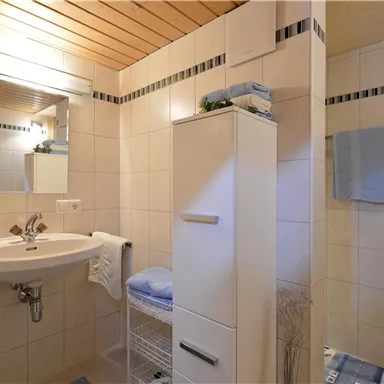 Ein modernes Badezimmer mit einem Waschbecken und einem Spiegel. Es gibt helle Fliesen und Handtücher in Blau und Weiß, die für ein frisches Ambiente sorgen.