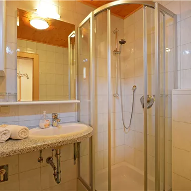 Ein modernes Badezimmer mit einer Duschkabine und einem Waschbecken. Frische Handtücher liegen bereit und die Wände sind hell gefliest.