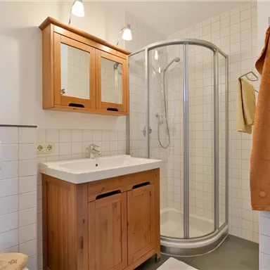 A modern bathroom with a shower and a wooden sink. Towels in soft colors hang on the wall.