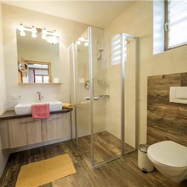 A modern bathroom with a shower and a sink. The walls are light, and the floor has an appealing wood design.