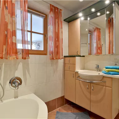 Ein modernes Badezimmer mit einer Badewanne und Dusche. Helle Farben und große Fenster sorgen für eine freundliche Atmosphäre.