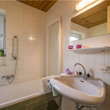 Ein Badezimmer mit einer Badewanne und einem Waschbecken. Helle Fliesen und ein Fenster sorgen für eine freundliche Atmosphäre.