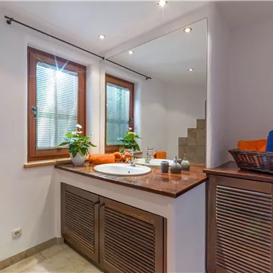 A modern bathroom with a sink and wooden cabinets. There are plants and towels in vibrant colors.