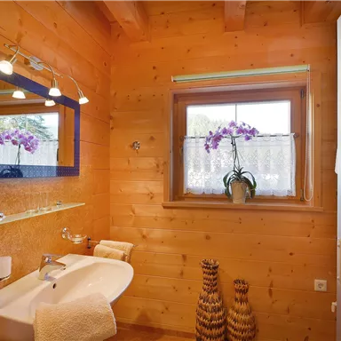 Ein modernes Badezimmer mit Holzverkleidung und großen Spiegeln. Auf der Fensterbank steht eine Orchidee und es gibt dekorative Elemente.