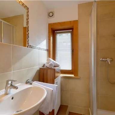 Ein modernes Badezimmer mit einer Dusche und einem Waschbecken. Helle Fliesen und ein Fenster sorgen für eine einladende Atmosphäre.