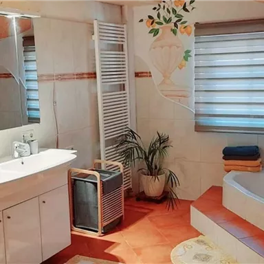A modern bathroom with a bathtub and a large mirror. The walls are bright, and there are plants as well as towels for an inviting atmosphere.