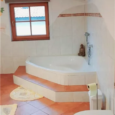 A modern bathroom with a round bathtub and a toilet. Large windows provide plenty of natural light.