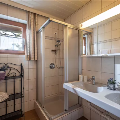 Ein modernes Badezimmer mit Dusche und Waschbecken. Helle Fliesen und natürliche Beleuchtung sorgen für eine freundliche Atmosphäre.