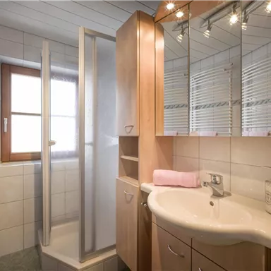 A modern bathroom with a shower and a sink. The walls are tiled in light colors and there are large mirrors.