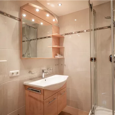 A modern bathroom with a glass shower and a sink. Bright tiles and tasteful lighting create an inviting atmosphere.