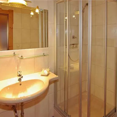 A modern bathroom with a shower cabin and a sink. The walls are brightly tiled, and there is a mirror above the sink.