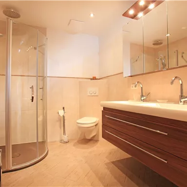 Ein modernes Badezimmer mit einer Dusche, einem großen Waschbecken und einem WC. Die hellen Fliesen und das Holzdesign schaffen eine einladende Atmosphäre.