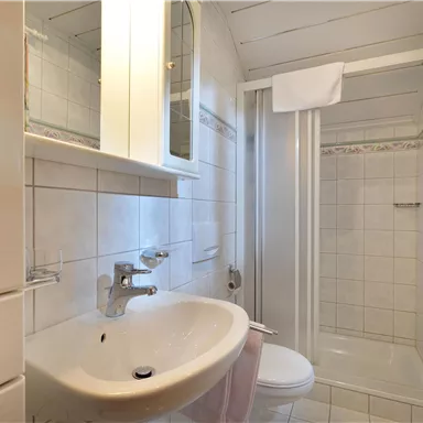 Ein modernes Badezimmer mit einer Dusche, einem Waschbecken und einem großen Spiegel. Die Wände sind mit weißen Fliesen gefliest und es gibt helles Licht.