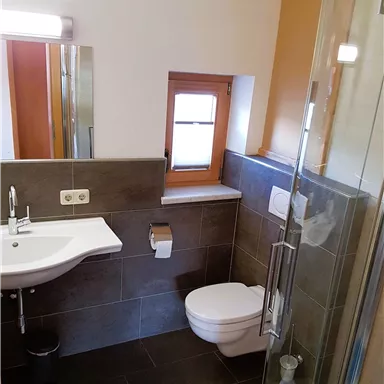 A modern bathroom with shower, sink, and toilet. Bright walls and large windows create a pleasant atmosphere.