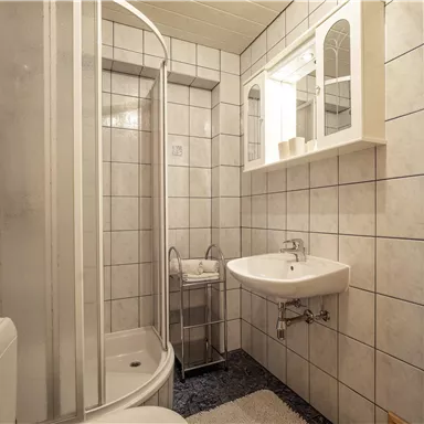 Ein modernes Badezimmer mit weißen Fliesen und einer Duschkabine. Es gibt ein Waschbecken und einen großen Spiegel.