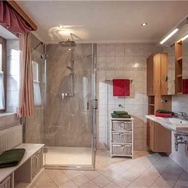 A modern designed bathroom with a glass shower and a bright tiled floor. The walls are tiled with light tiles, and there are decorative towels in red and green.