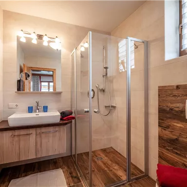 A modern bathroom with a glass shower cabin and a sleek sink. The walls are in neutral tones, complemented by wooden elements.