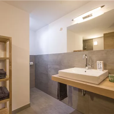 Ein modernes Badezimmer mit einer eleganten Waschbeckenplatte und einer großen Spiegel. Die Wände sind in neutralen Farben gehalten und Handtücher sowie Kerzen sorgen für eine einladende Atmosphäre.