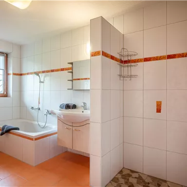 A bright bathroom with a bathtub and a shower. The walls are tiled, and there is a window that lets in light.
